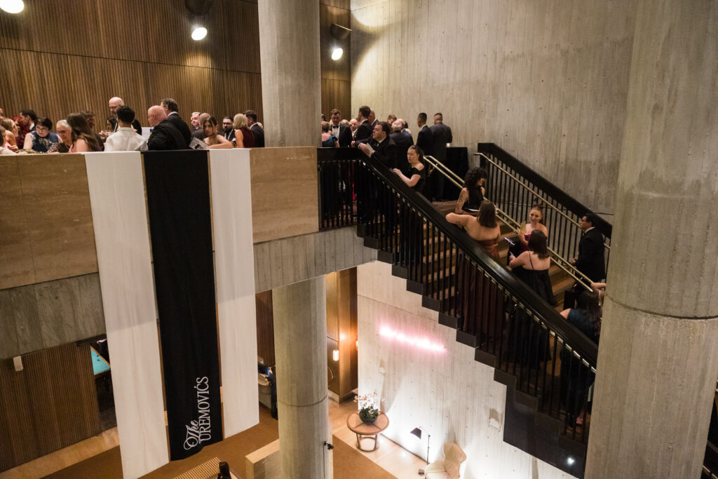 Formal event in a modern concrete atrium with guests mingling along a black staircase and balconies.